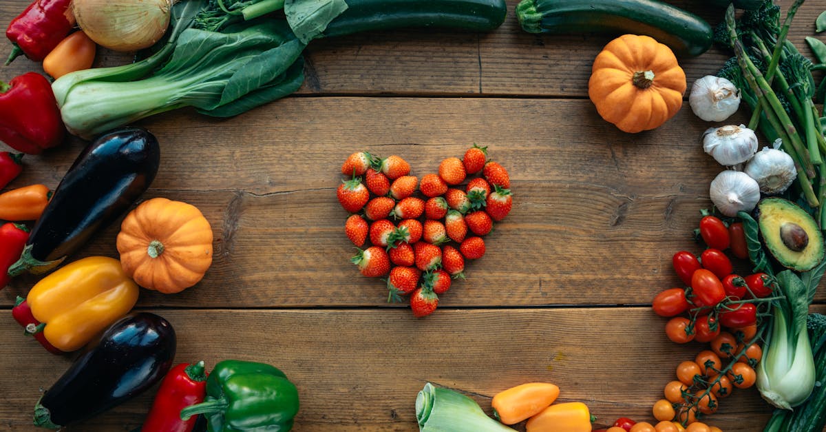 Vibrant fruits and vegetables arranged heart-shaped on a wooden surface, top view.