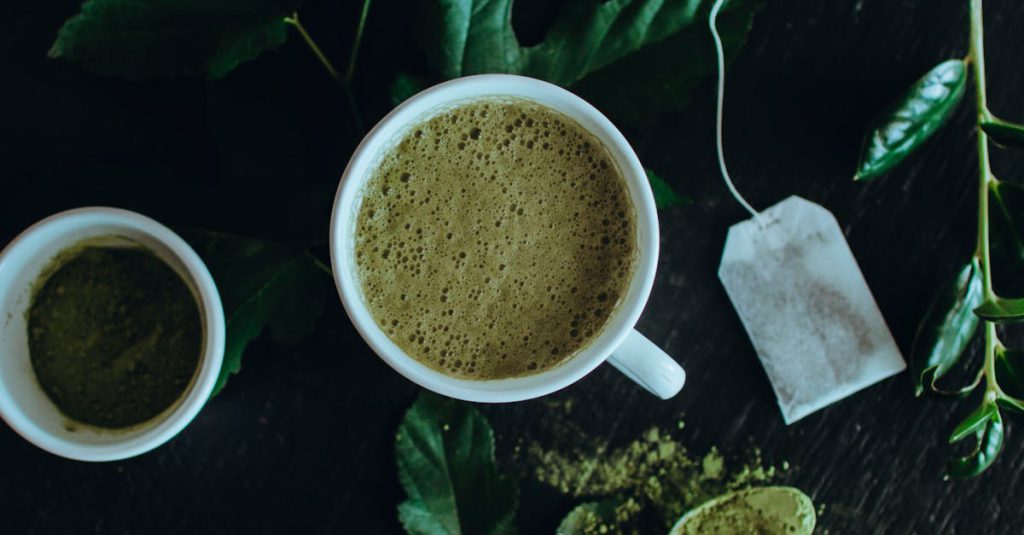 pexels-photo-5168515-5168515 Top view of a refreshing matcha latte surrounded by leaves, powder, and a tea bag.