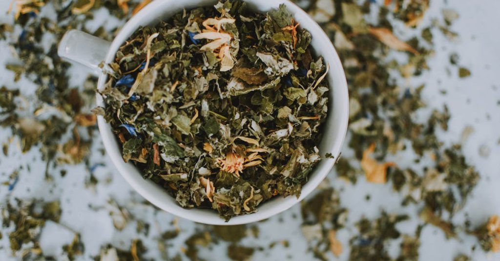 Overhead shot of a cup with a blend of dried herbal tea leaves and flowers.
